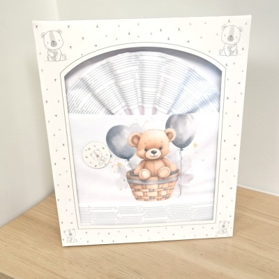 Conjunto de roupa de bebé com urso e balões numa caixa branca decorada com ursos e estrelas.