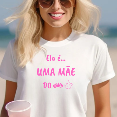 T-shirt branca com texto em rosa e ícones, usada por mulher loira com óculos de sol na praia