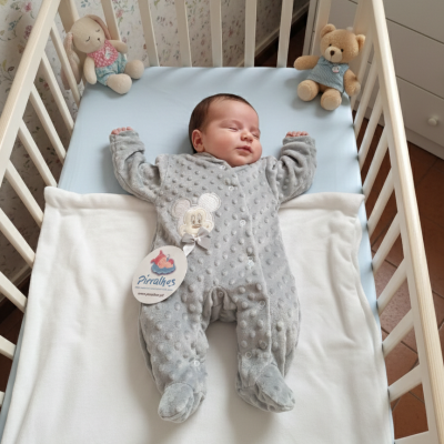 Berço com bebé vestido de fato cinzento com textura, manta branca e peluches