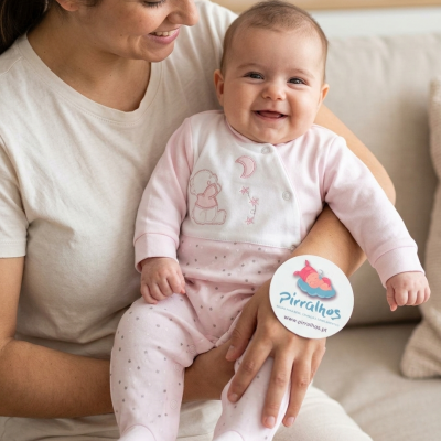 Bebé sorridente em pijama rosa claro no colo de uma mulher com camiseta bege