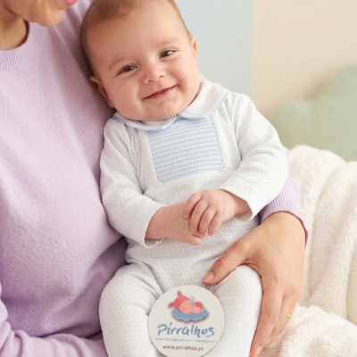 Bebé com fato branco com pontos azuis e etiqueta Pirralhos sentado no colo de adulto com camisola lilás