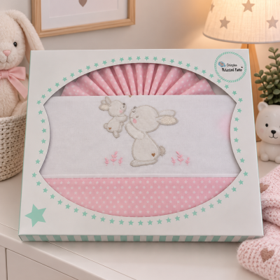 Conjunto de roupa de bebé rosa com coelhos bordados numa caixa branca decorada com estrelas verdes