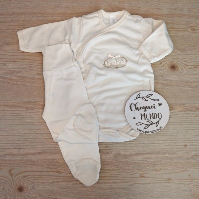 Conjunto branco de roupa para bebé com body de mangas compridas e calças com pés, em algodão, sobre fundo de madeira.