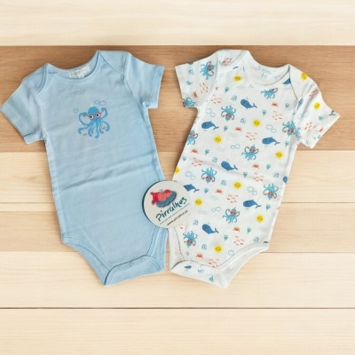 Dois bodies de bebé com estampas marinhas sobre superfície clara de madeira