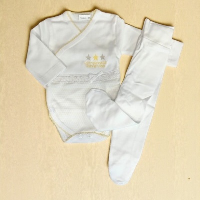 Conjunto de roupa de bebé branco com body e meia-calça sobre superfície bege.