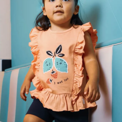 Criança com camisa cor de pêssego com folhos e estampa de folhas e calções escuros