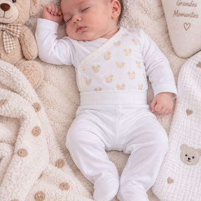 Bebé a dormir vestido com roupa branca estampada numa manta bege felpuda com pontos castanhos