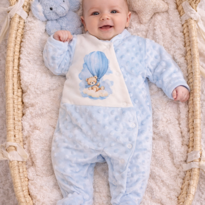 Bebé deitado numa cama de vime com fato de pijama azul claro e boneco de peluche azul