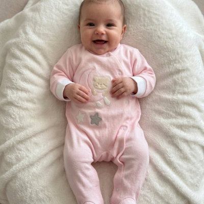 Macacão rosa para bebé com ursinho bordado sobre almofada branca macia.