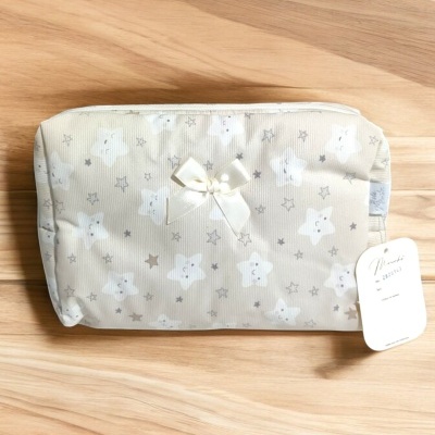 Necessaire bege com padrão de estrelas e nuvens e laço decorativo, sobre mesa de madeira