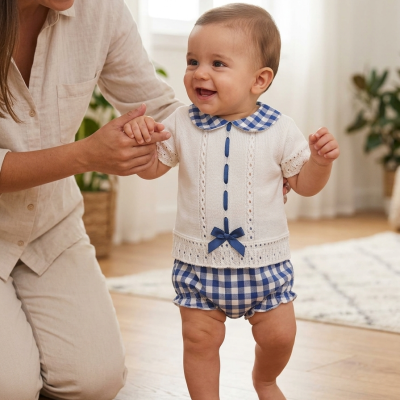 Bebé com roupa branca e azul às quadrículas a andar dentro de casa com ajuda de uma mulher.