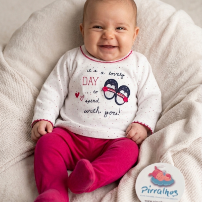 Bebé de manga comprida com camisola branca e calças rosas sentado numa manta creme macia.