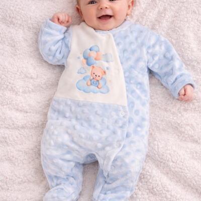 Bebé deitado com macacão azul claro e painel branco estampado com ursinho e balões.
