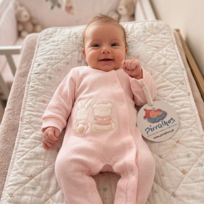 Bebé com pijama cor de rosa de malha com desenhos de coelho e urso deitada em almofada acolchoada com padrão de estrelas