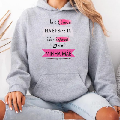 Mulher sentada a usar sweatshirt cinza clara com capuz e texto colorido sobre mães.