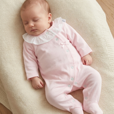 Bebé dormindo com macacão rosa claro com gola branca sobre mantinha bege
