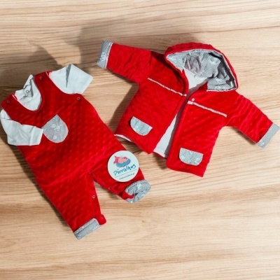 Conjunto de roupa de bebé vermelho e branco com etiquetas, sobre chão de madeira