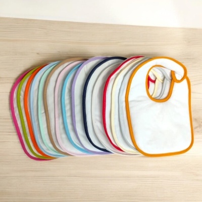 Babetes para bebé brancos com bordas coloridas dispostos em leque sobre madeira clara