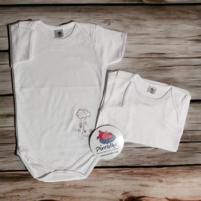 Dois bodies de bebé brancos com um pequeno estampado e um botão promocional sobre madeira