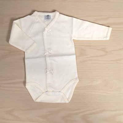 Body bebé creme de manga comprida com laços e molas sobre fundo madeira.