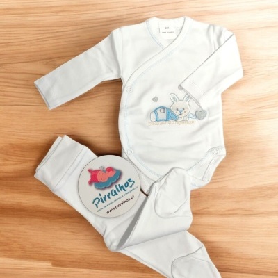 Conjunto de roupa de bebé branco com body e calças com pezinhos sobre madeira clara