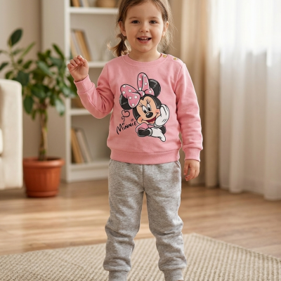 Criança de pijama com estampa da Minnie em sala de estar com tapete e brinquedo de comboio.