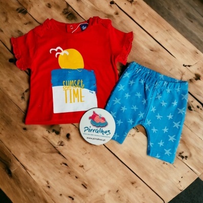 Conjunto infantil com t-shirt vermelha e bermuda azul sobre mesa de madeira