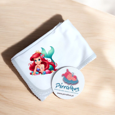 Lenço branco com estampa de sereia e etiqueta redonda de marca Pirralhos em superfície de madeira