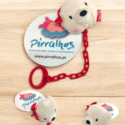 Brinquedo de pelúcia em forma de cabeça de urso com corrente vermelha e etiqueta da marca Pirralhos