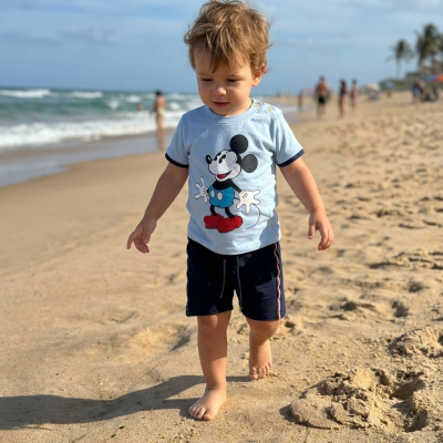 Menino descalço na praia com t-shirt do Mickey Mouse azul