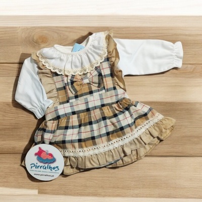 Vestido infantil xadrez com detalhes rendados e calças brancas sobre mesa de madeira clara
