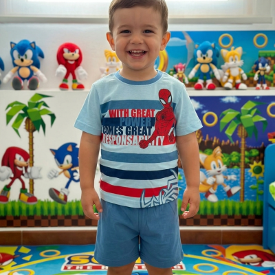 Camisola de criança azul clara com Homem-Aranha e texto, calções azuis, criança sorridente num quarto com decoração do Sonic.