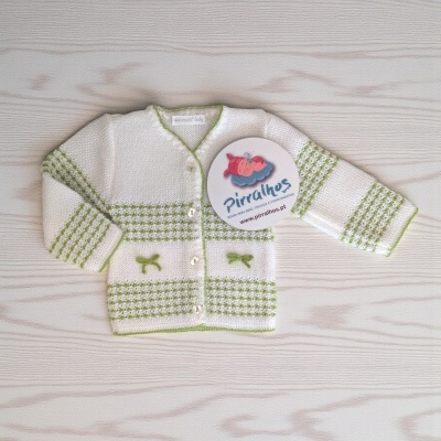 Camisola de bebé branca com padrões verdes e botões, sobre uma superfície de madeira clara.