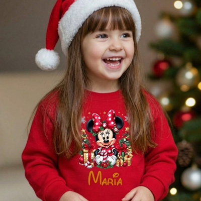 Criança com suéter vermelho de Minnie Mouse natalício e gorro de Papai Noel perto da árvore de Natal