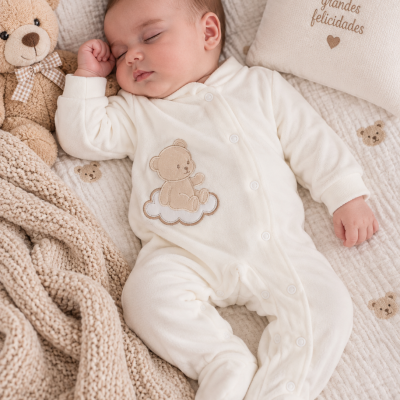 Bebé a dormir com pijama branco e ursinho de peluche à esquerda