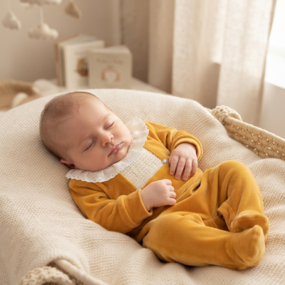 Bebé vestido com pijama amarelo deitado numa cesta de vime com cobertor bege