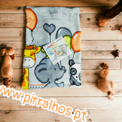 Manta infantil colorida com desenhos de animais e balões sobre chão de madeira com peluches castanhos