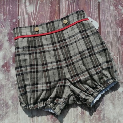Calção infantil xadrez cinza com detalhes vermelhos e botões em fundo de madeira vinho