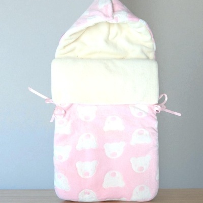 Saco de bebé rosa com padrão de ursinhos brancos e capuz, tecido polar, fundo cinzento e madeira