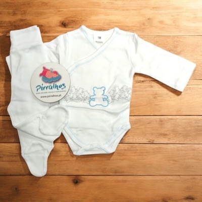 Conjunto roupa bebé branco com ursinho azul e calças com pé, sobre madeira clara