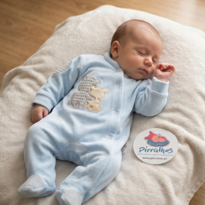 Bebé de pijama azul claro com ursos, deitado em almofada branca felpuda com etiqueta Pirralhos ao lado.