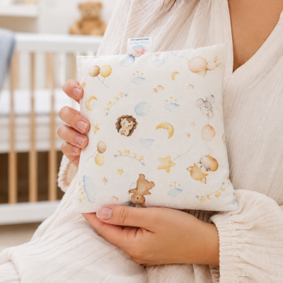 Almofada infantil com estampa de animais e elementos celestiais segura por pessoa em quarto de bebé