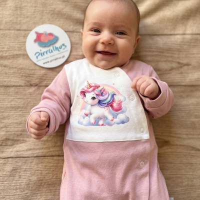 Bebé sorridente vestido com macacão rosa e branco com desenho de unicórnio.