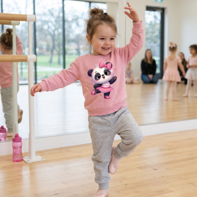 Menina a dançar em estúdio de ballet com sweatshirt rosa estampada e calças cinzentas