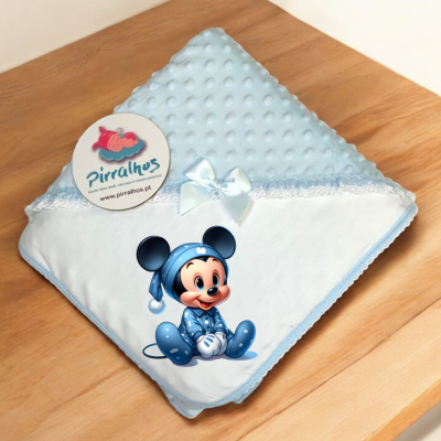 Manta de bebé azul com laço branco e rato Mickey em pijama azul sobre mesa de madeira