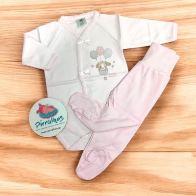 Conjunto de roupa de bebé branco e rosa com desenho de cão e balões, sobre fundo de madeira