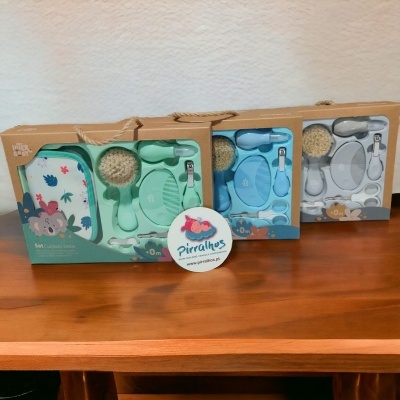 Três conjuntos de cuidados para bebé em embalagens de cartão, cores verde, azul e cinza, com escova, pente, esponja e estojo, com padrão infantil e texto '0+m'.