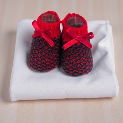 Sapatinhos de bebé vermelhos e pretos com laços vermelhos sobre pano branco