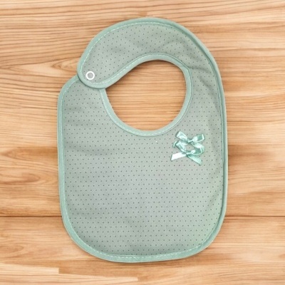 Babeiro verde-água com pontos pequenos e laços, sobre superfície de madeira