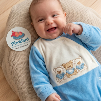 Bebé sorridente com macacão azul e creme junto a etiqueta Pirralhos